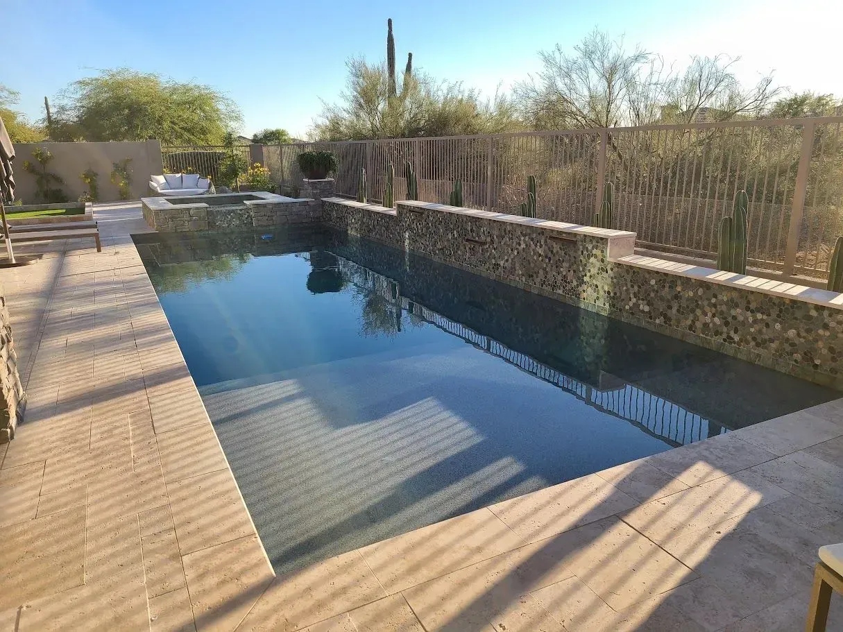 Rectangular pool with dark water beside a wooden deck and desert landscaping in bright sunlight