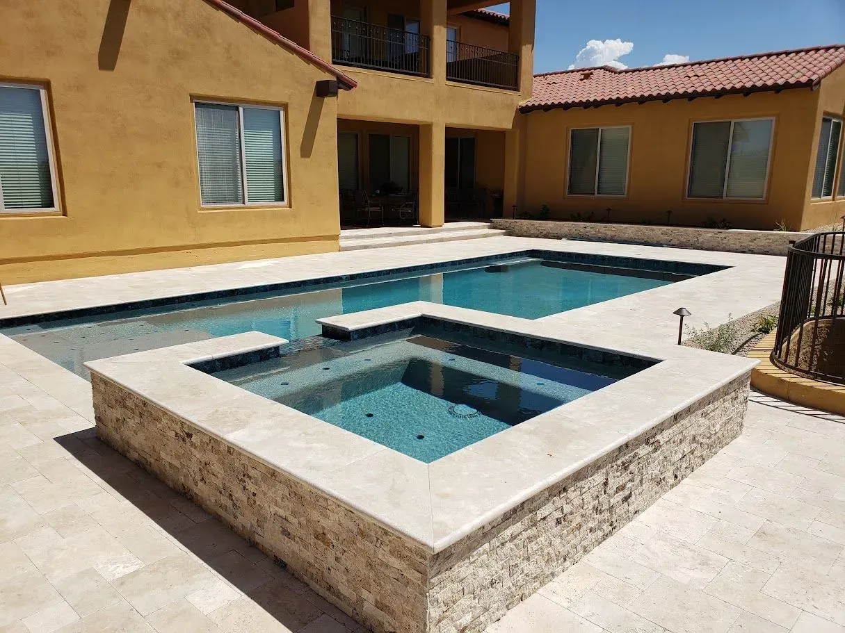 Courtyard pool with a raised square spa and blue water beside a tan stucco building.
