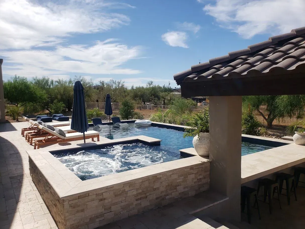 Backyard pool with lounge chairs, blue umbrellas, and a covered outdoor bar under a sunny sky