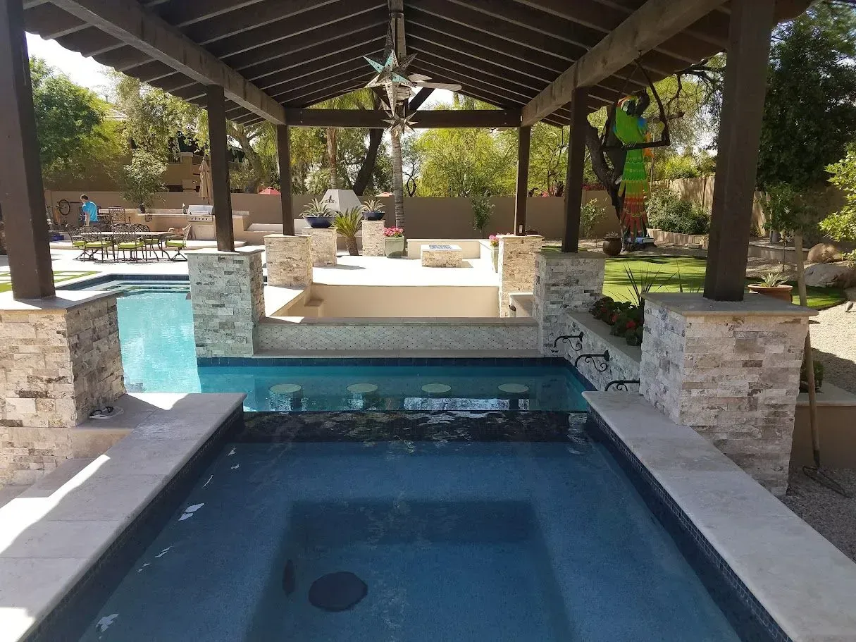Covered outdoor pool with stone accents and a hot tub under a pavilion