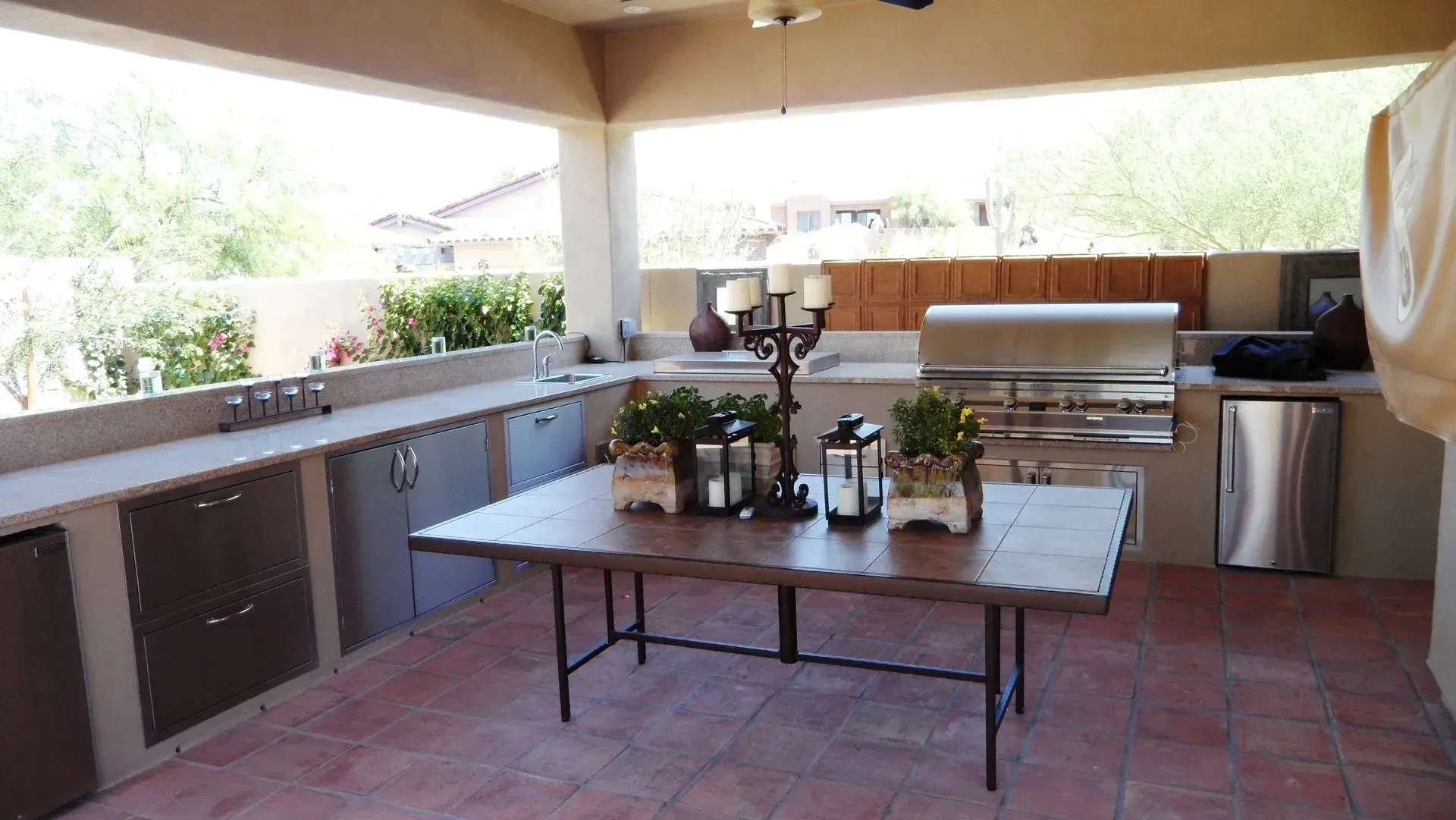 Covered outdoor patio with a grill, sink, dining table, and potted plants