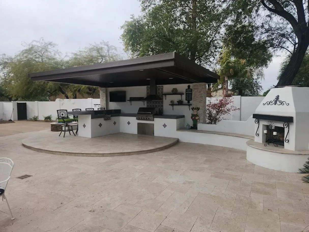 Outdoor patio with a covered grill station, fire pit, and seating area beneath trees