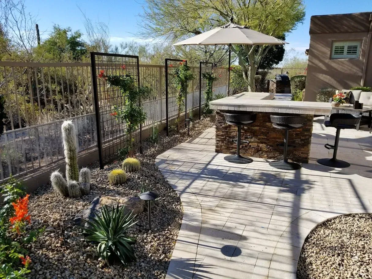 Desert garden patio with cactus beds, a stone walkway, umbrella, and built-in grill area.
