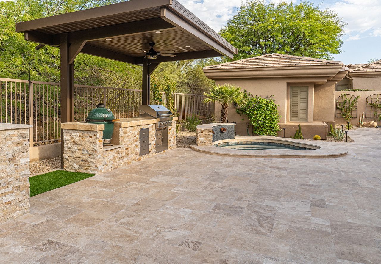 Stone outdoor pavilion with a dark wooden roof, built-in grill, and bench seating.