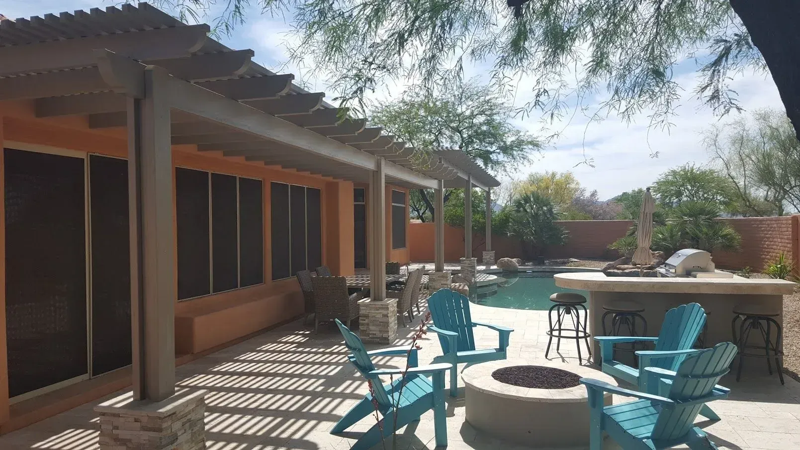 Patio with turquoise chairs and fire pit beside a shaded house, under bright daylight.
