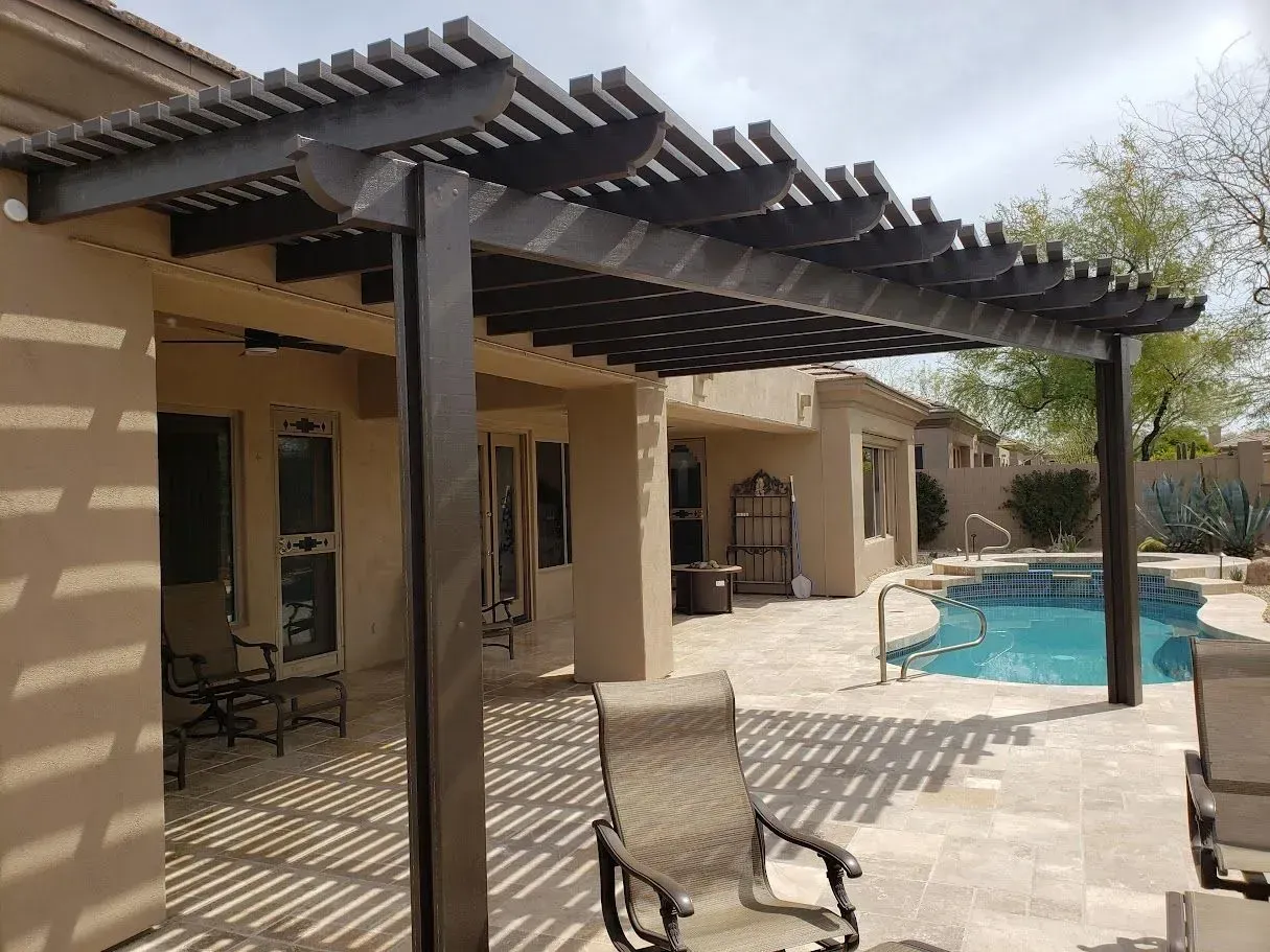 Patio with pergola beside a turquoise swimming pool at a desert-style house