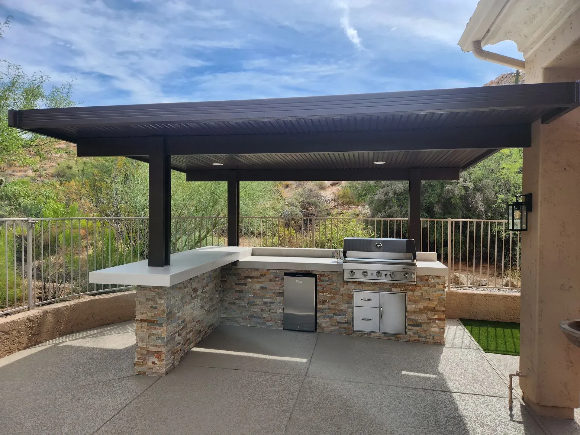 Outdoor patio with stone grill island, built-in barbecue, and dark-roofed pergola overlooking a yard