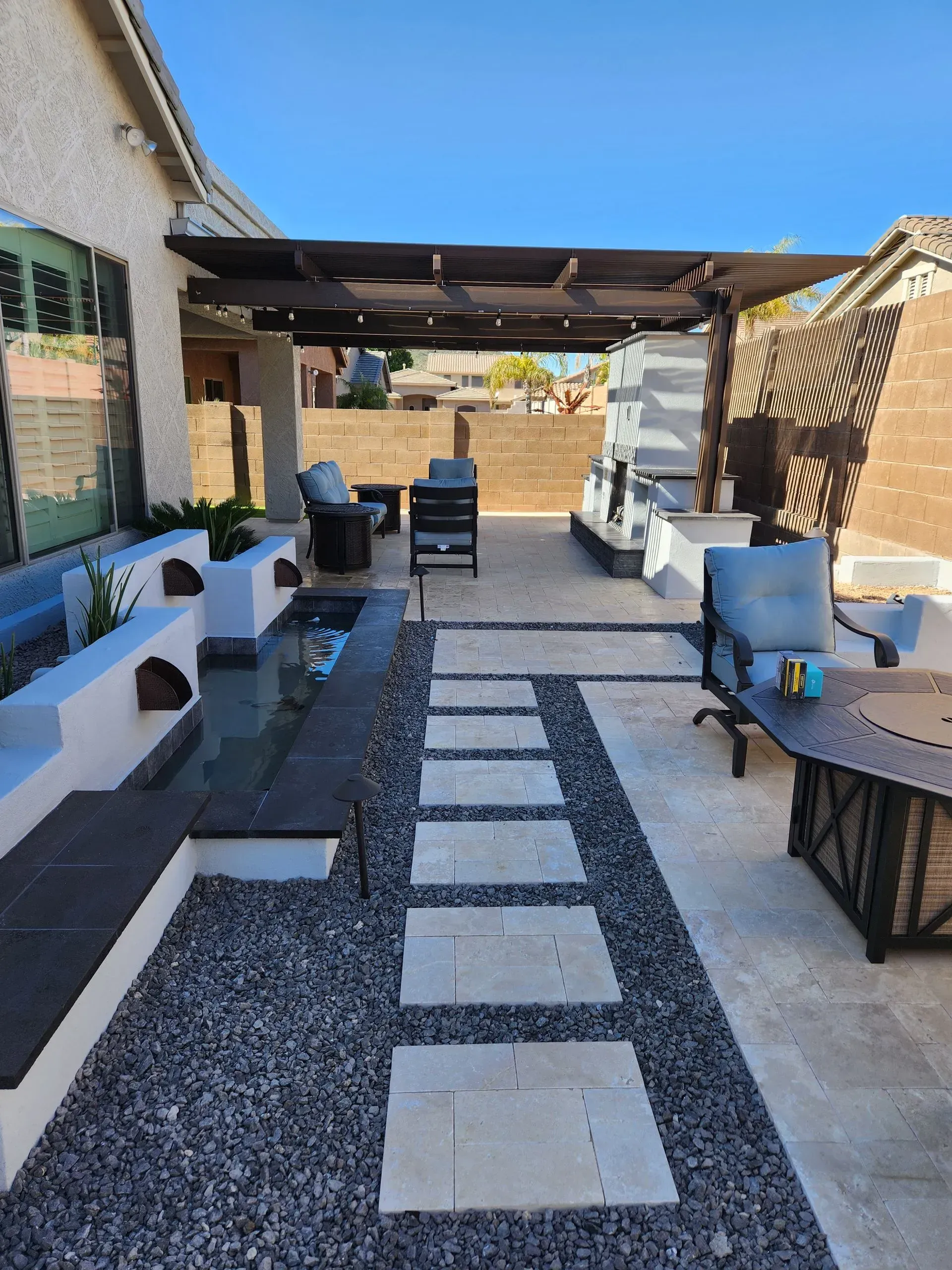 Covered outdoor patio with white benches, black tables, and a tiled stone walkway under a wooden pergola.