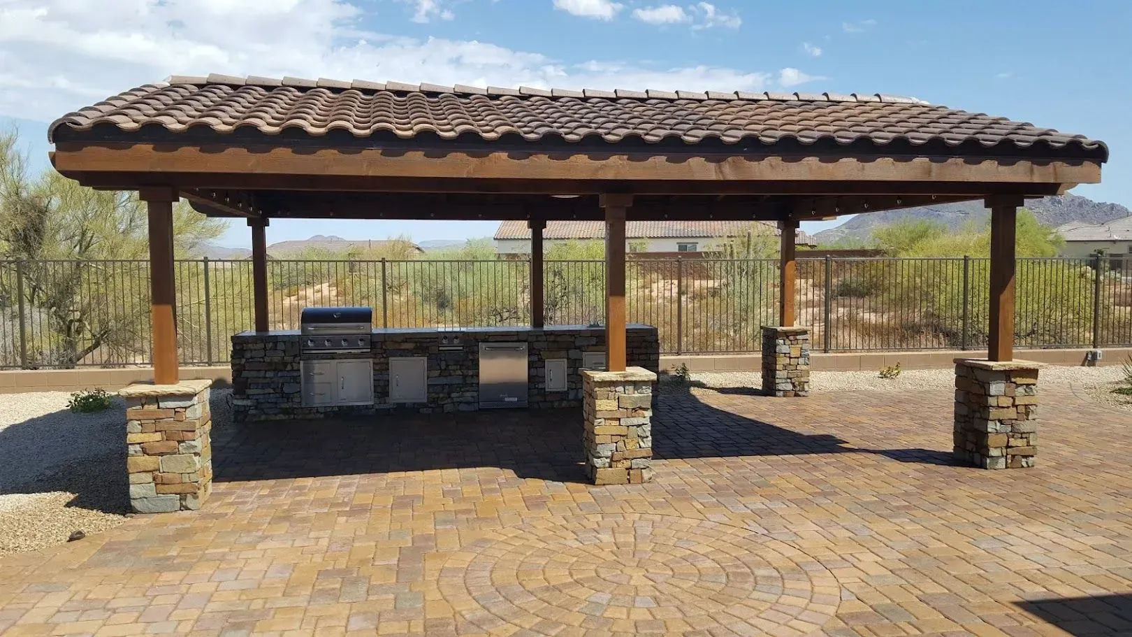 Open-air stone pavilion with a tiled roof and picnic tables in a sunny desert park