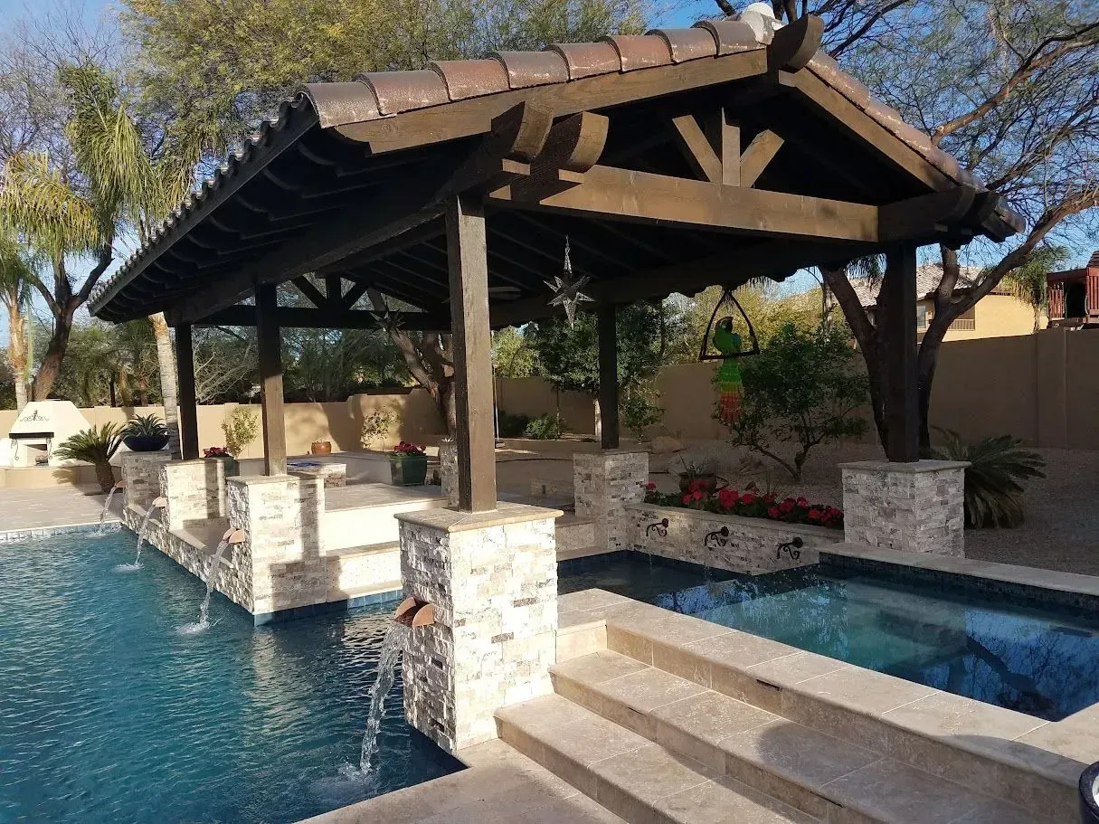 Backyard pool with a shaded wooden cabana, stone columns, and steps leading into the water