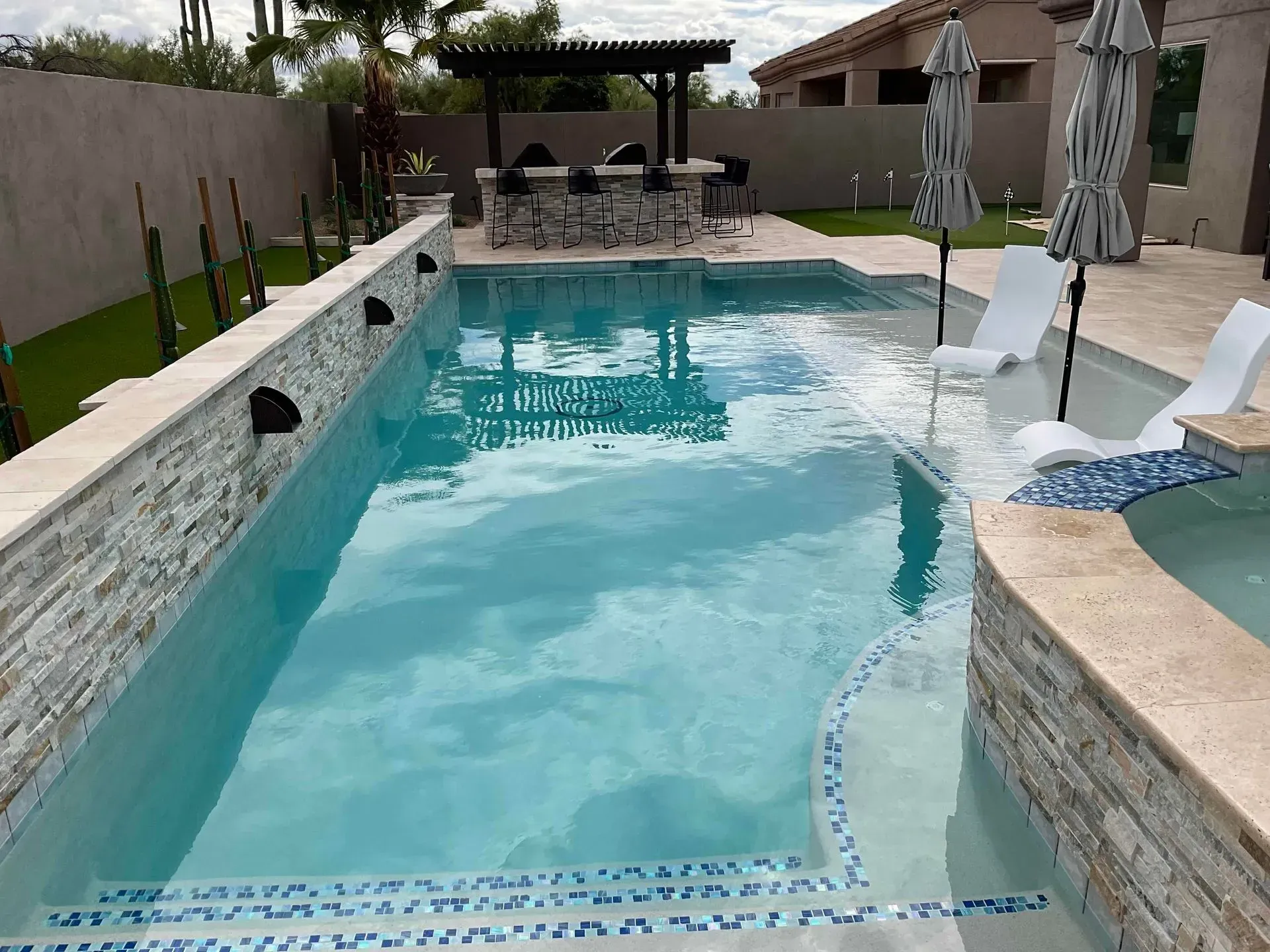 Backyard swimming pool with turquoise water, stone deck, lounge chairs, and covered patio seating