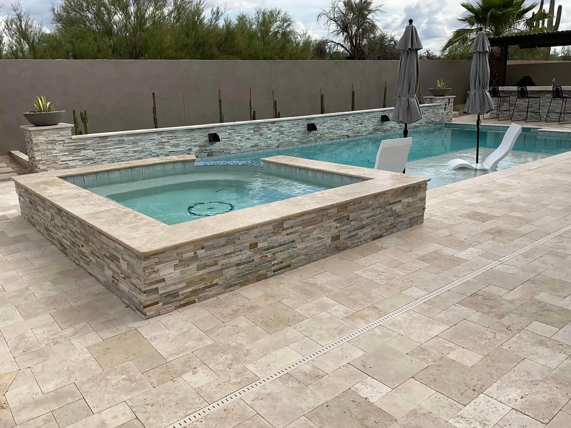 Modern backyard with a raised stone hot tub and pool beside a tiled patio.