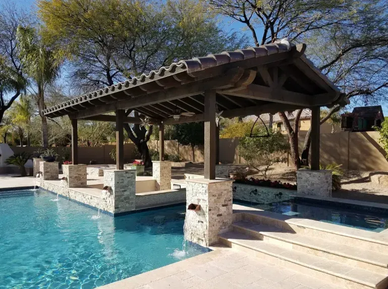 Poolside cabana with stone columns, turquoise water, and desert trees in the background