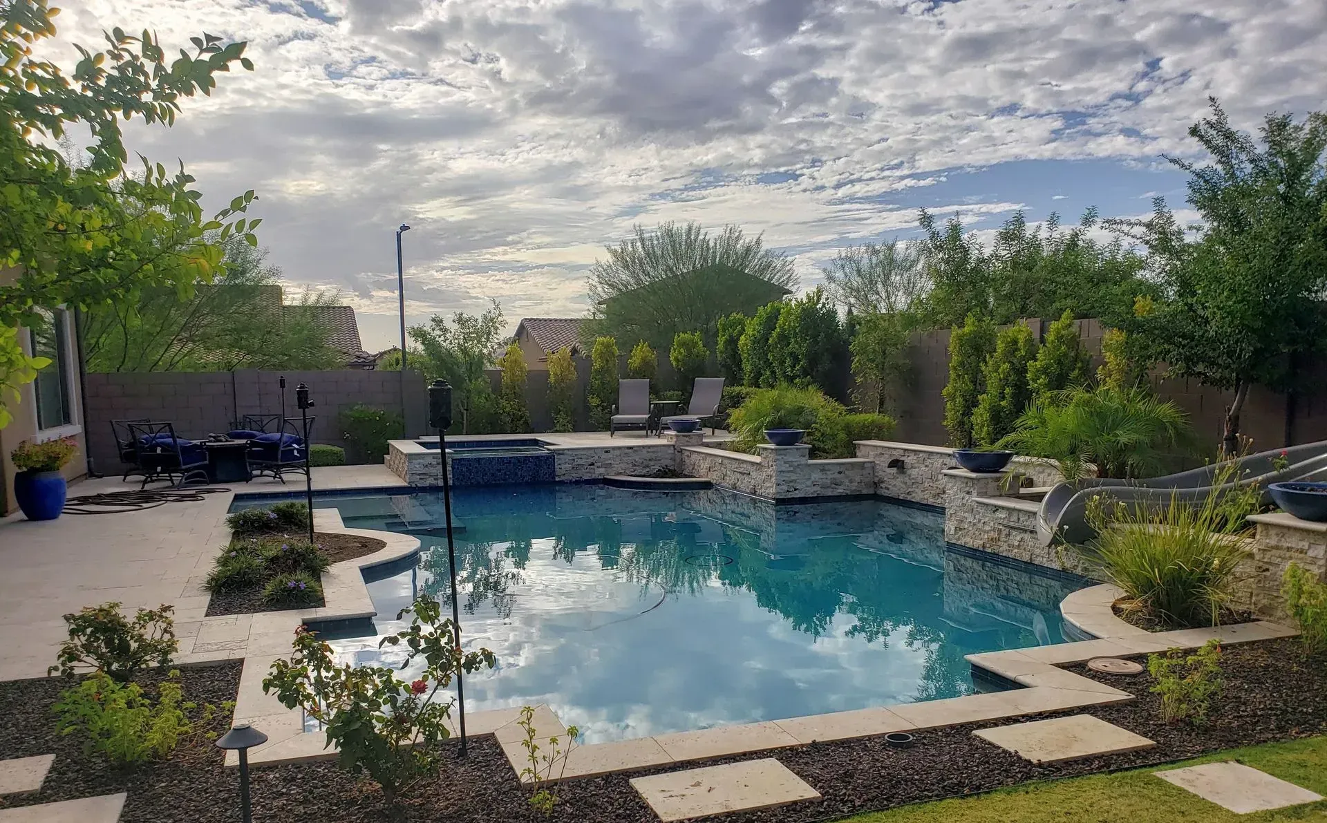 Backyard pool with stone landscaping, trees, and a cloudy sky reflection