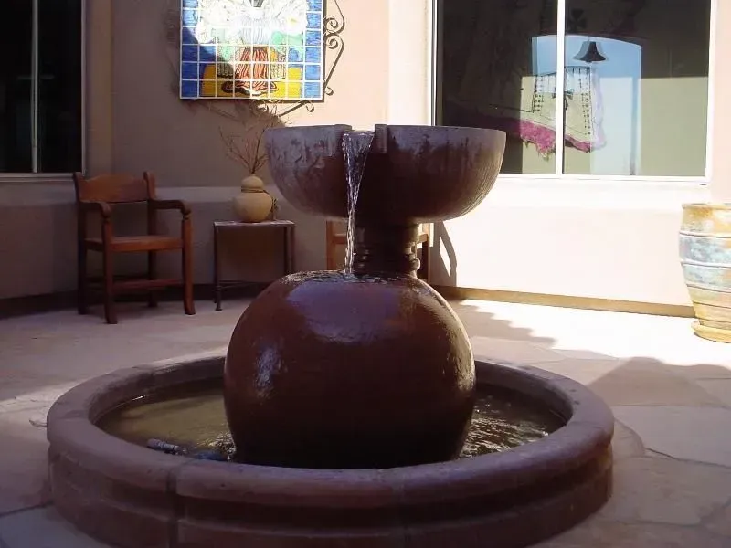 Dark ceramic fountain bowl in a courtyard with tiled floor, chairs, and a windowed wall