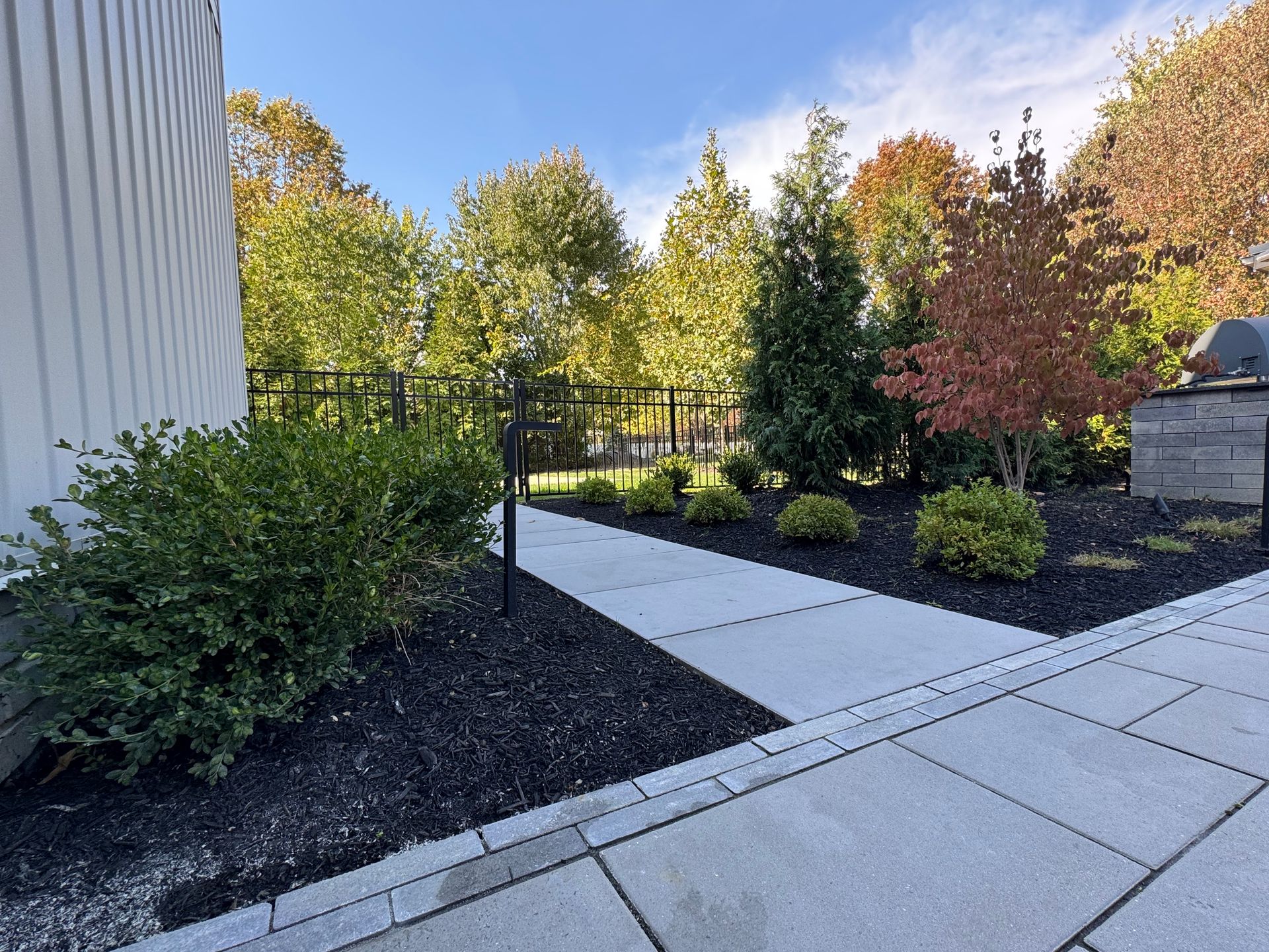 A paved walkway leads through a landscaped garden with green and red foliage.