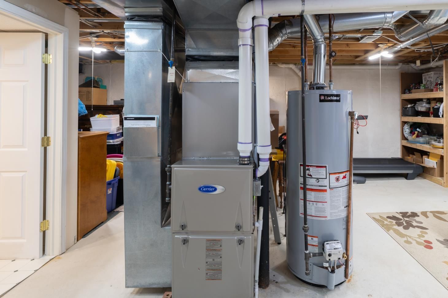 Basement with furnace, water heater, and ductwork. White door on the left, treadmill and shelving on the right.