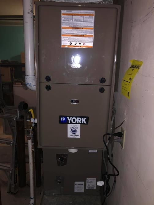 A York furnace in a room, featuring a beige exterior and connected piping and electrical components.