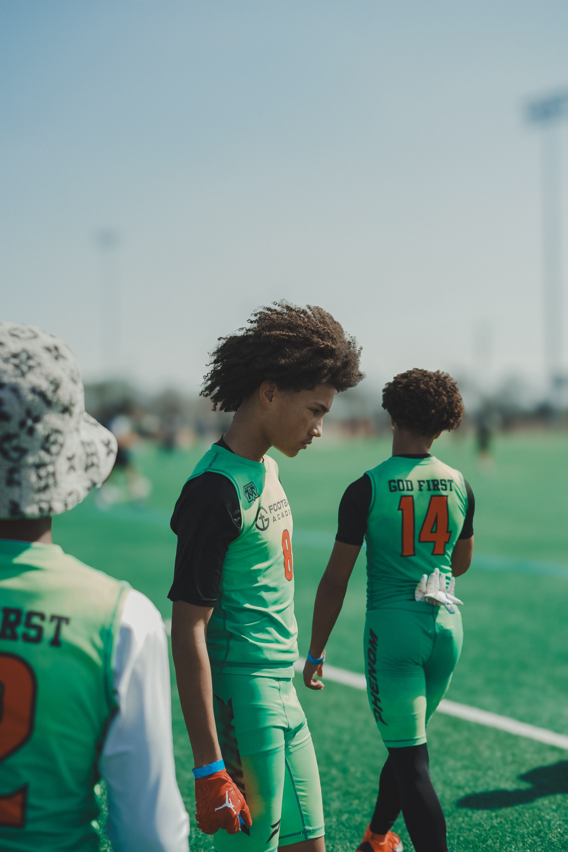 Soccer players in green uniforms standing on the field, one wearing number 14.