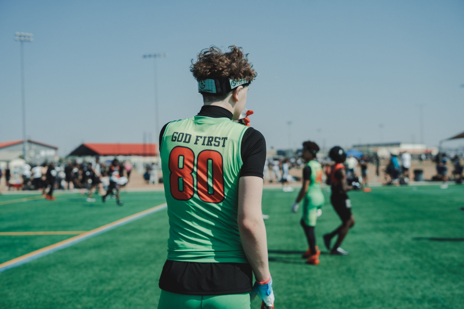Soccer player in green jersey with number 80 stands on a field, facing away from the camera