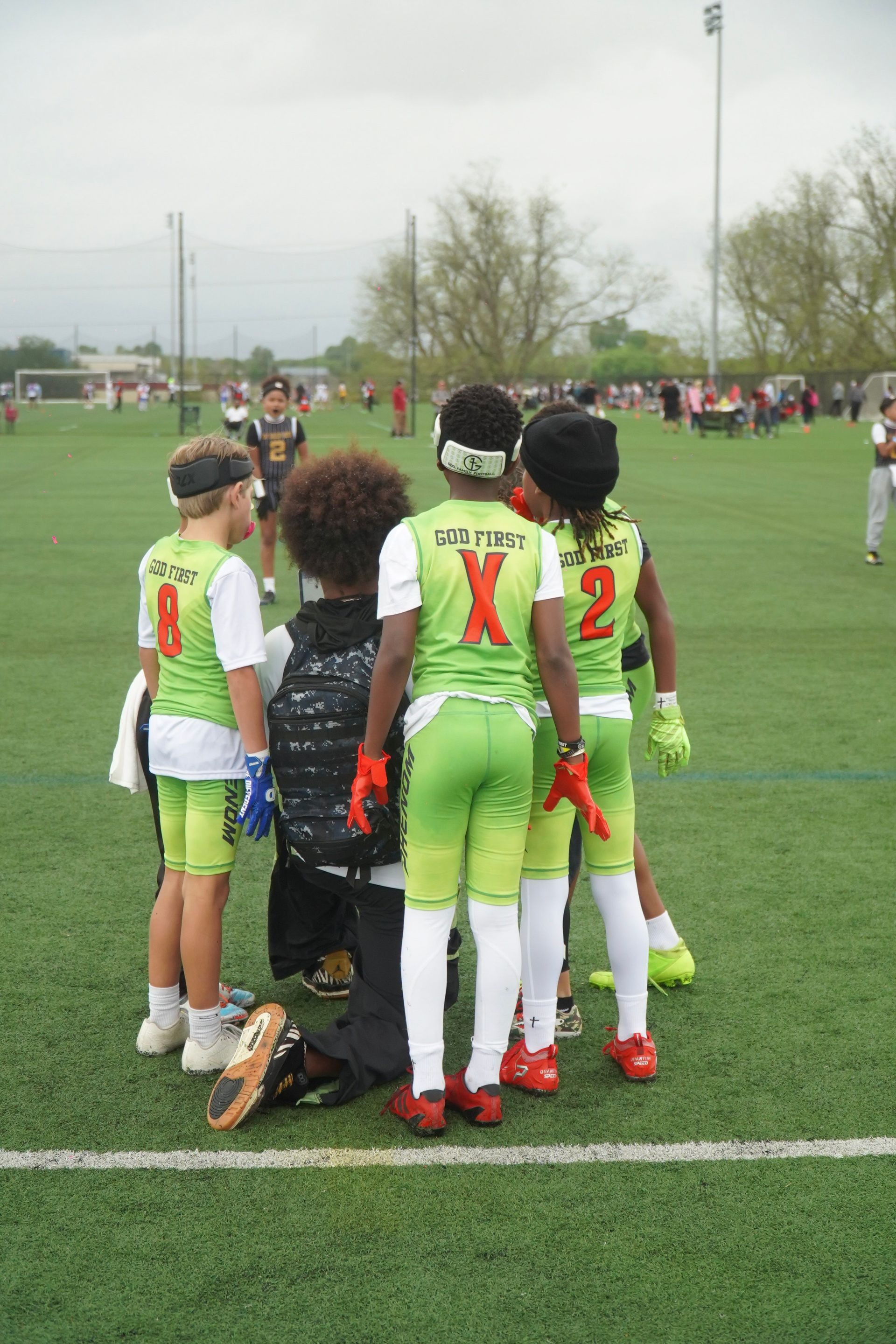 Youth soccer players huddle on a field, wearing neon green uniforms with red numbers.