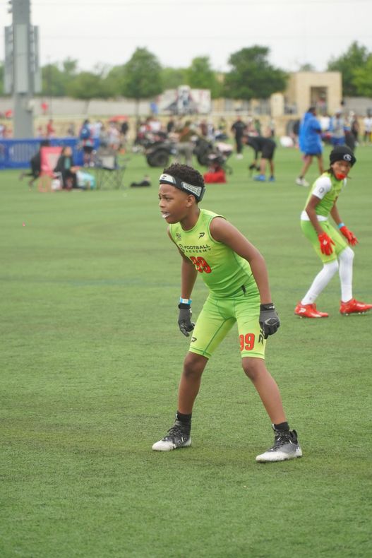 Two youth soccer players in green uniforms on a field, ready to play, with spectators in the background