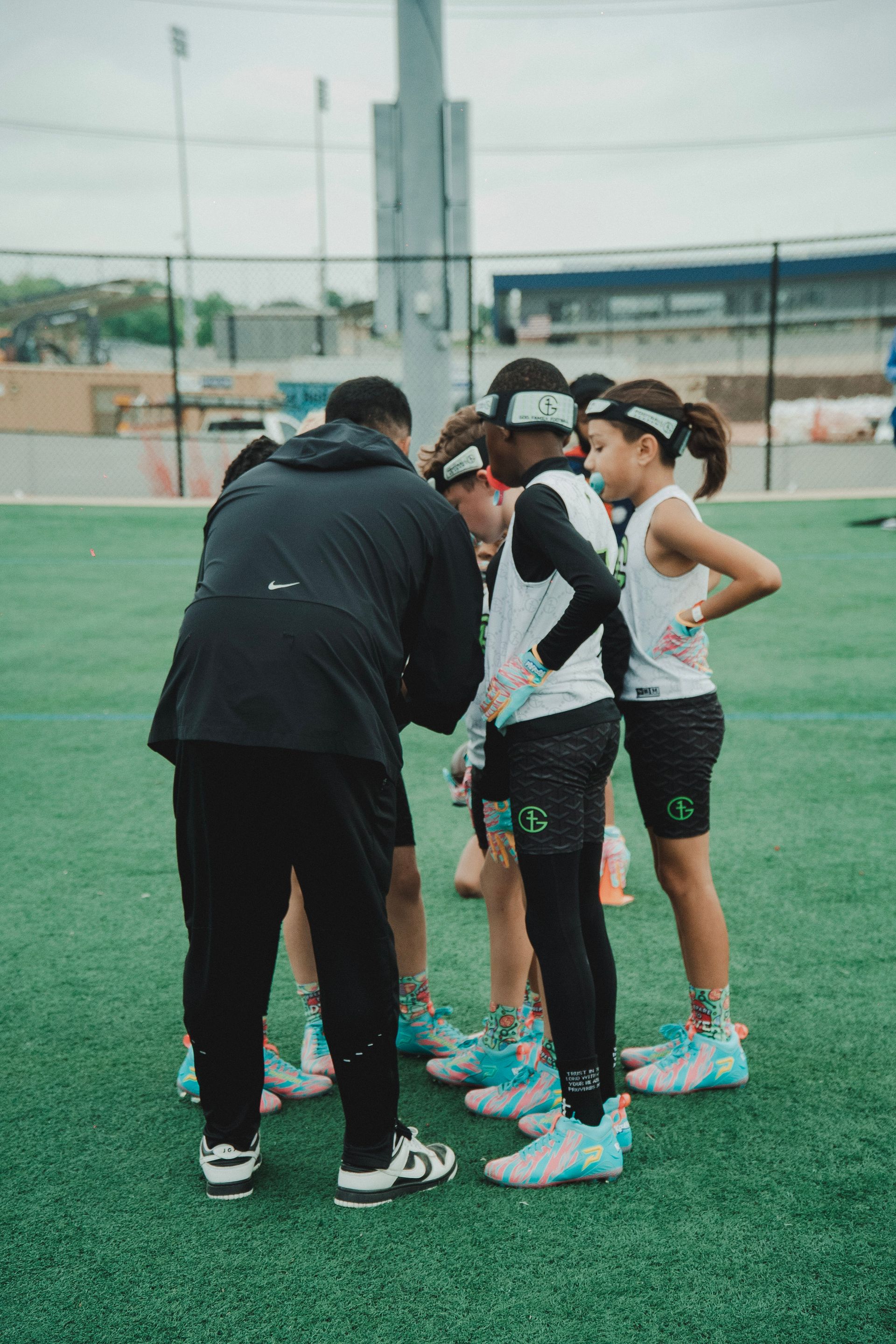 Coach briefs a group of five athletes on a turf field during practice.