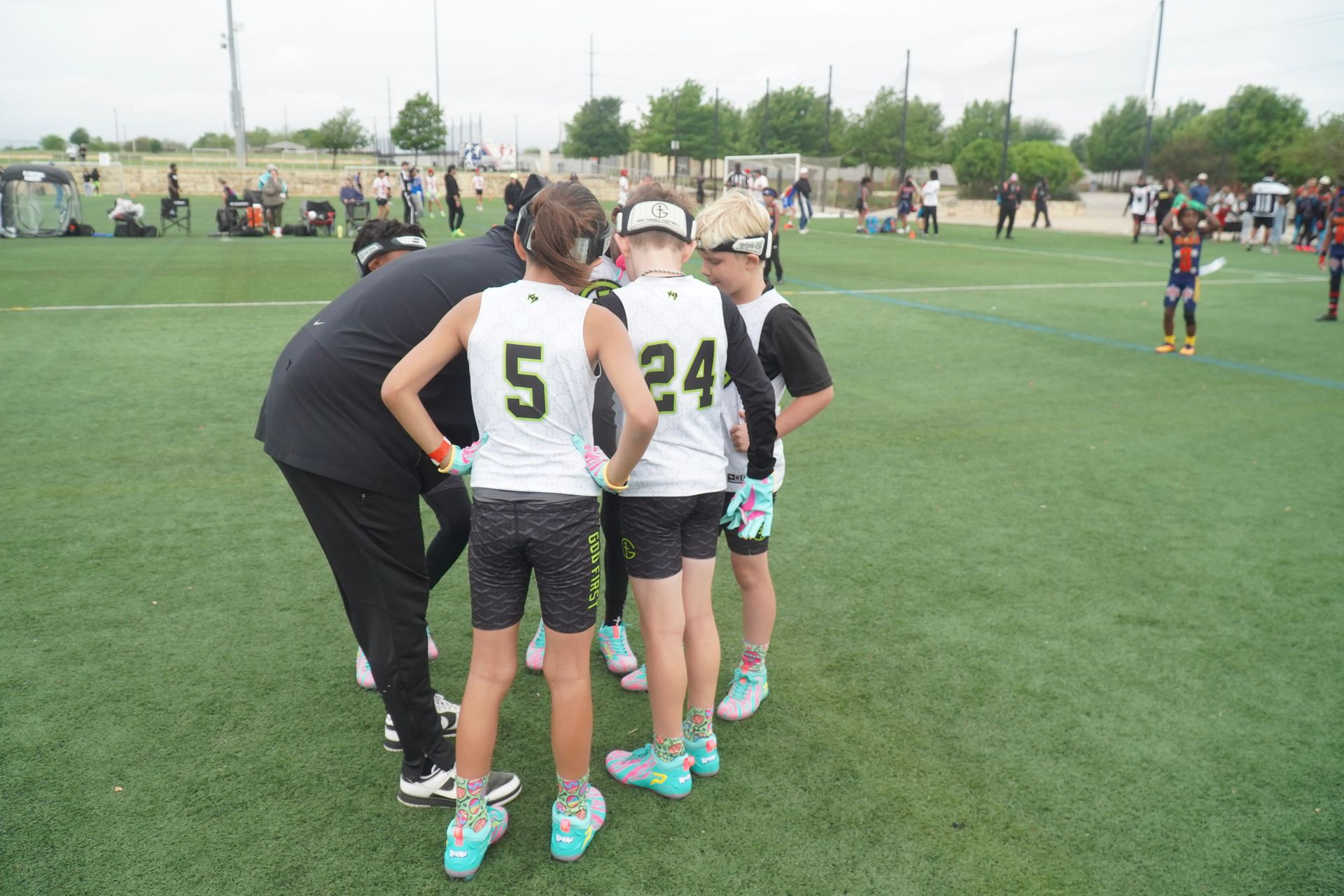 Youth soccer players huddle on a green field, with jerseys numbered 5 and 24 visible.