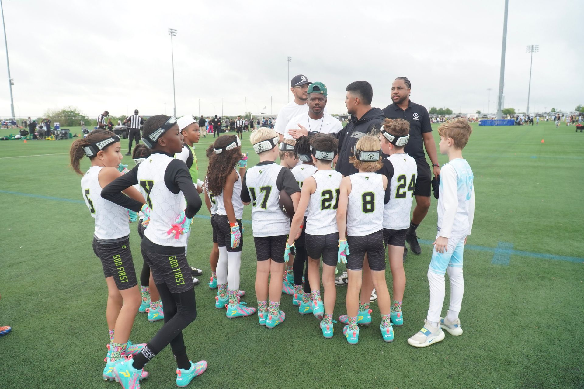 Youth soccer team huddles with coaches on a green field before practice.
