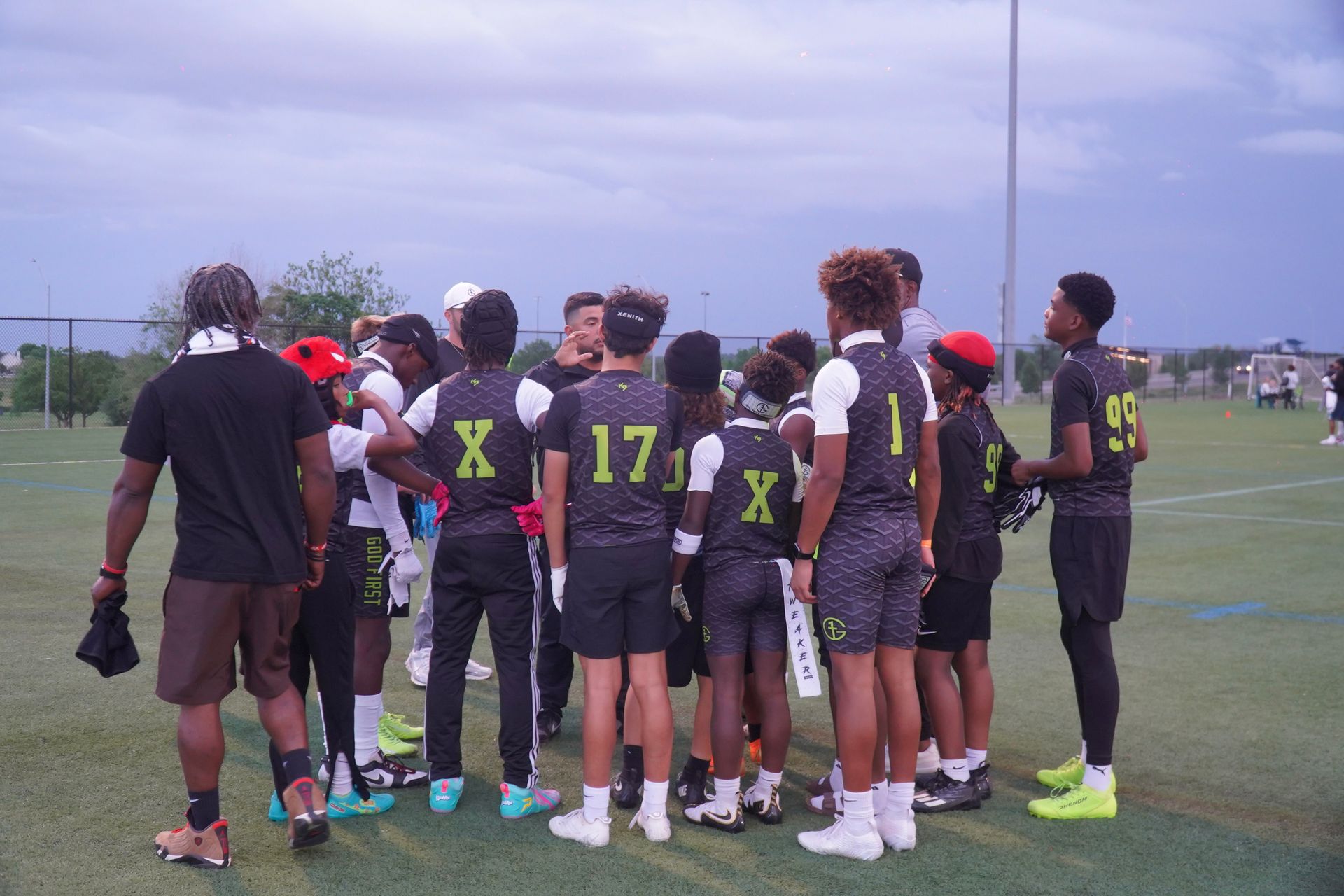 Soccer team huddled on a field before practice, wearing black uniforms with bright numbers.