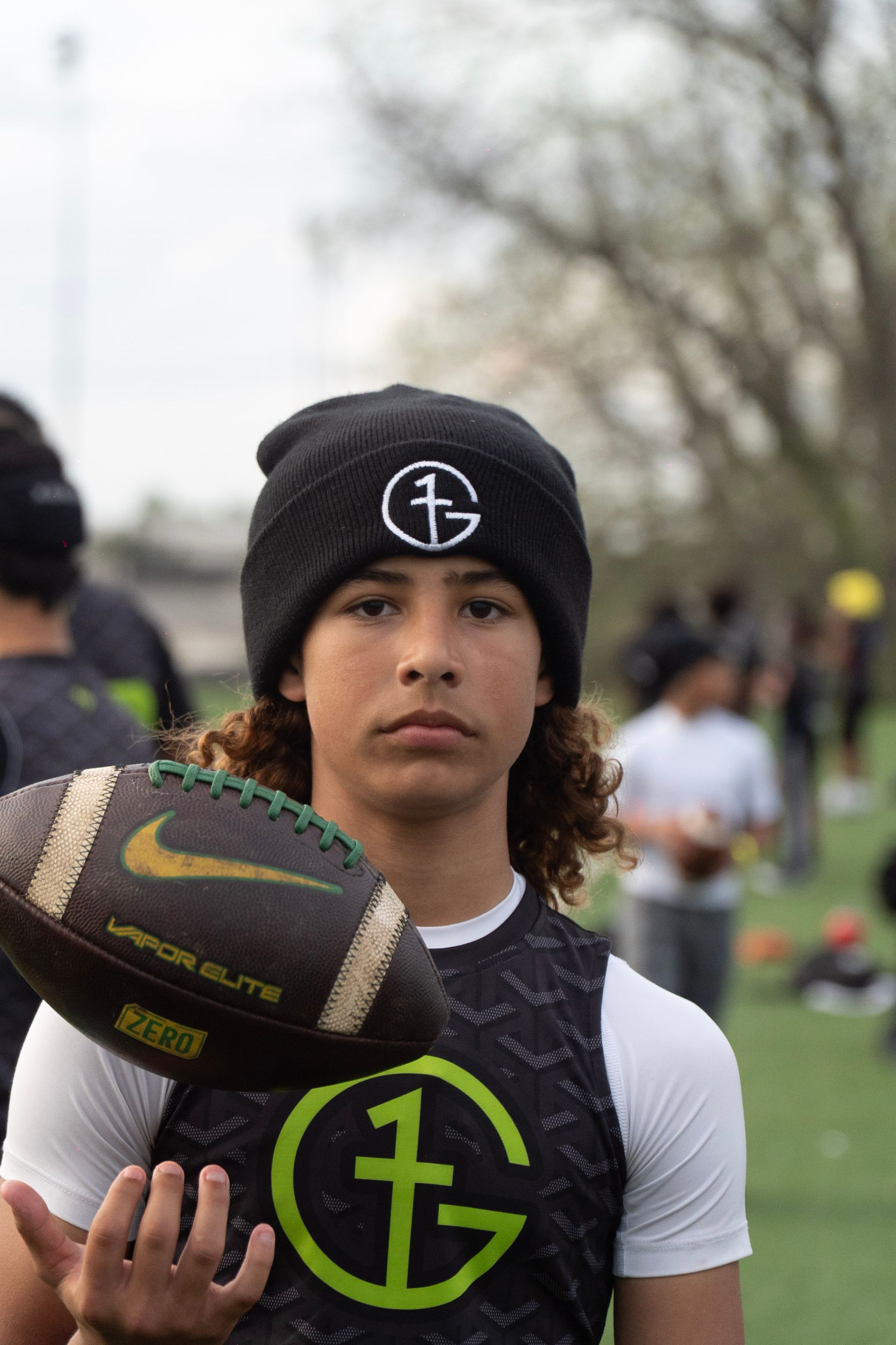 Football player holding a football, wearing a black beanie and black-and-white jersey outdoors