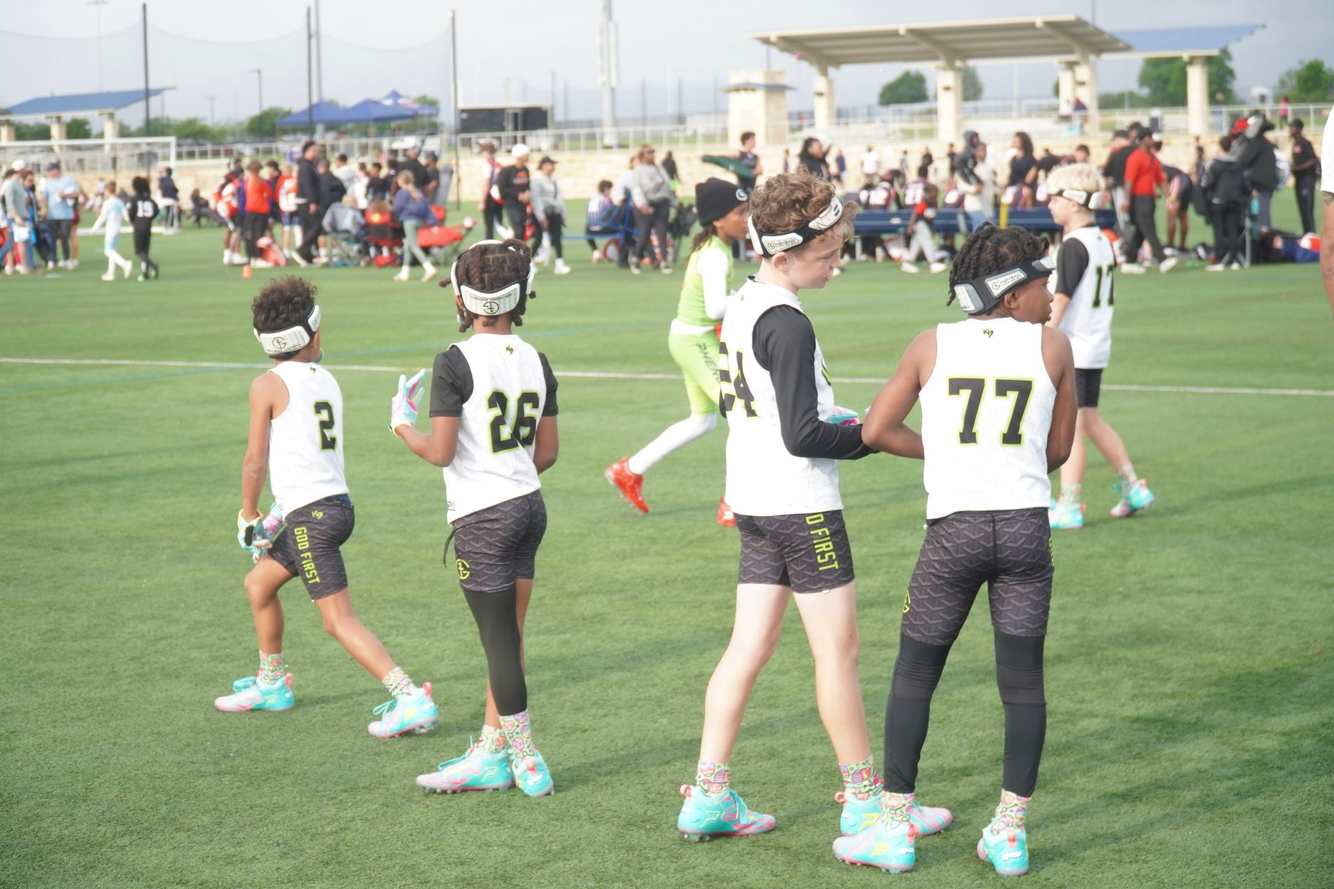 Soccer players in white jerseys walk on a field during a match, with spectators in the background