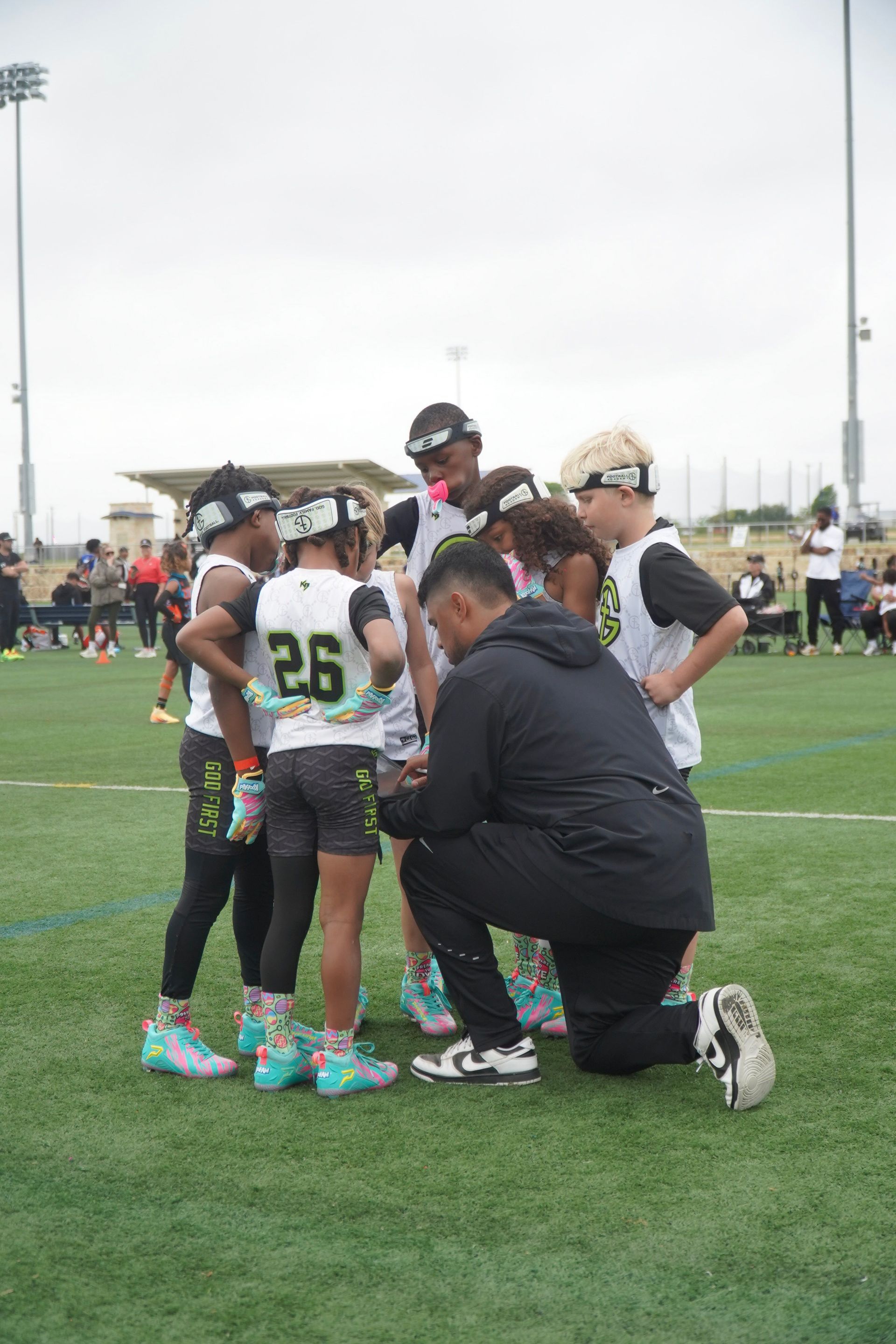 Youth football team huddles with a coach kneeling on the field during a game timeout.