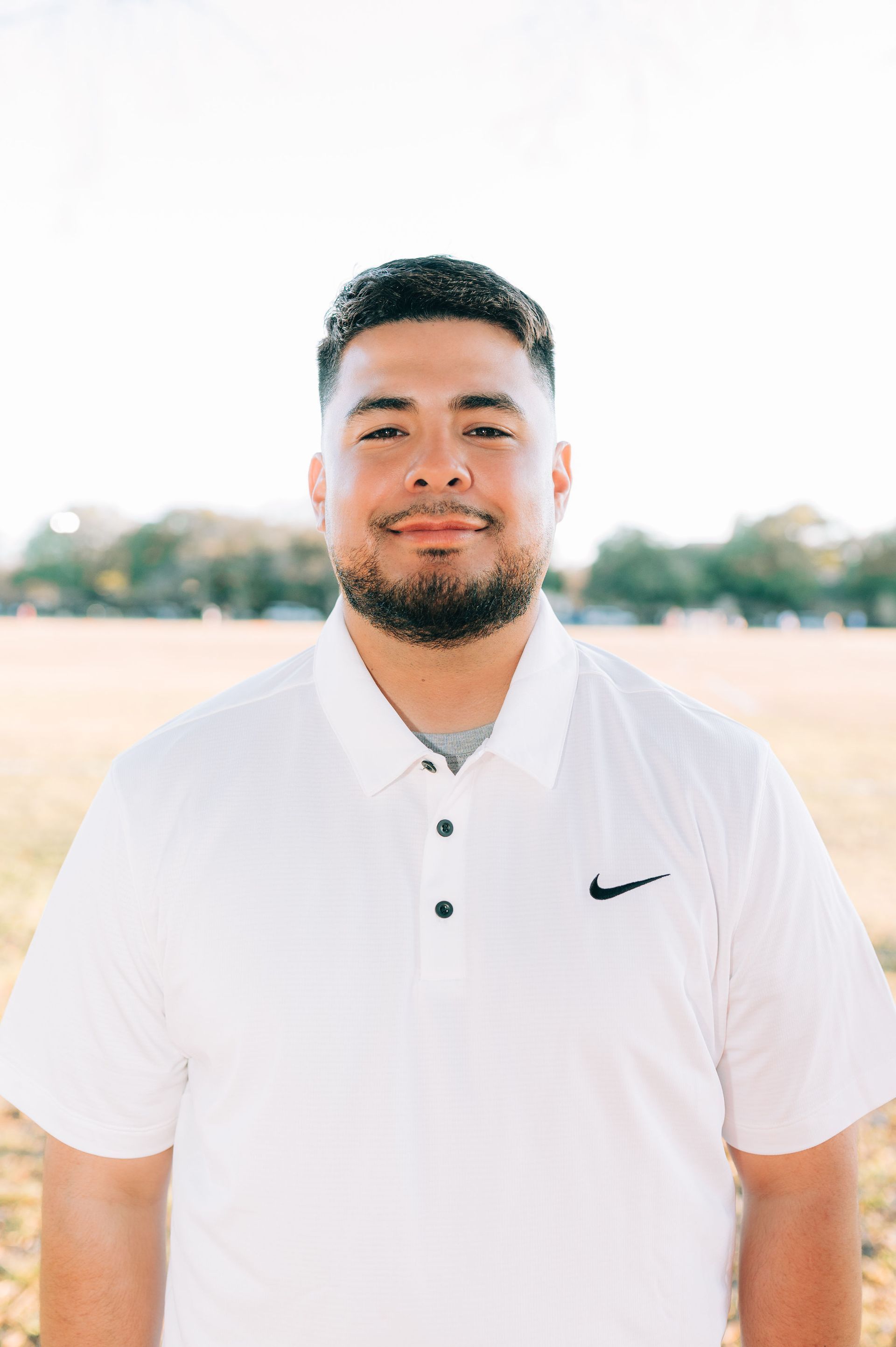 Man standing outdoors in a white Nike polo shirt, smiling at the camera.