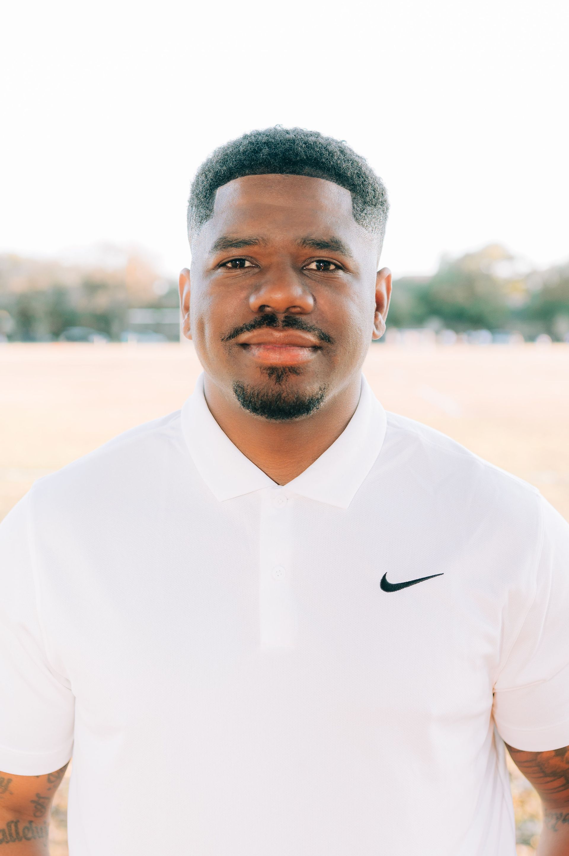 Portrait of a man in a white Nike polo shirt, standing outdoors with a neutral expression.