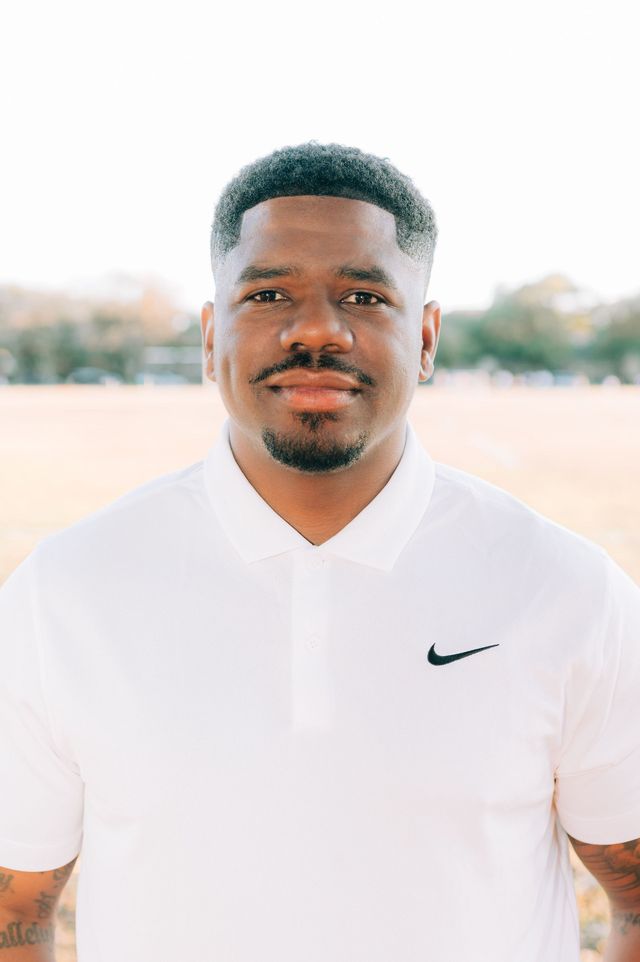 Portrait of a man in a white Nike polo shirt, standing outdoors with a neutral expression.