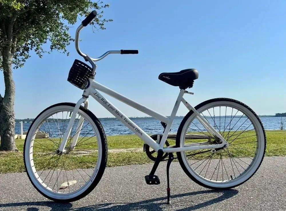 White beach cruiser bicycle parked on a paved path, overlooking a body of water.