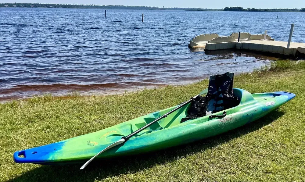 Green and blue kayak on grassy shore near a lake and dock. Paddle in kayak.