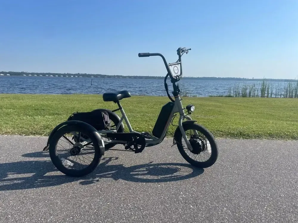 Electric tricycle on a paved path by water, sunny day.