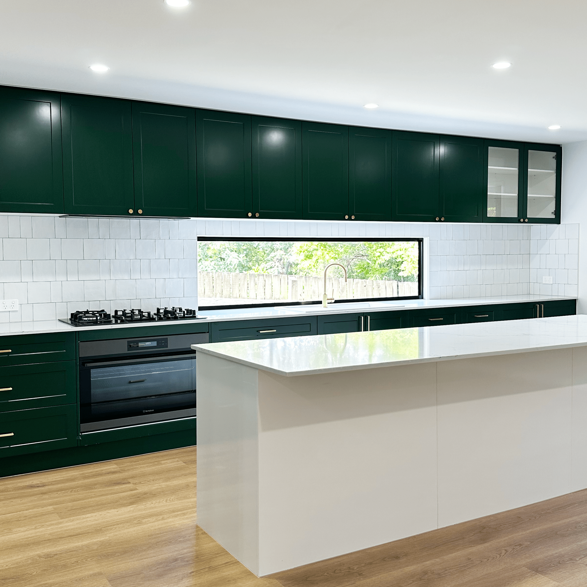 A kitchen with green cabinets , white counter tops , and a large island.