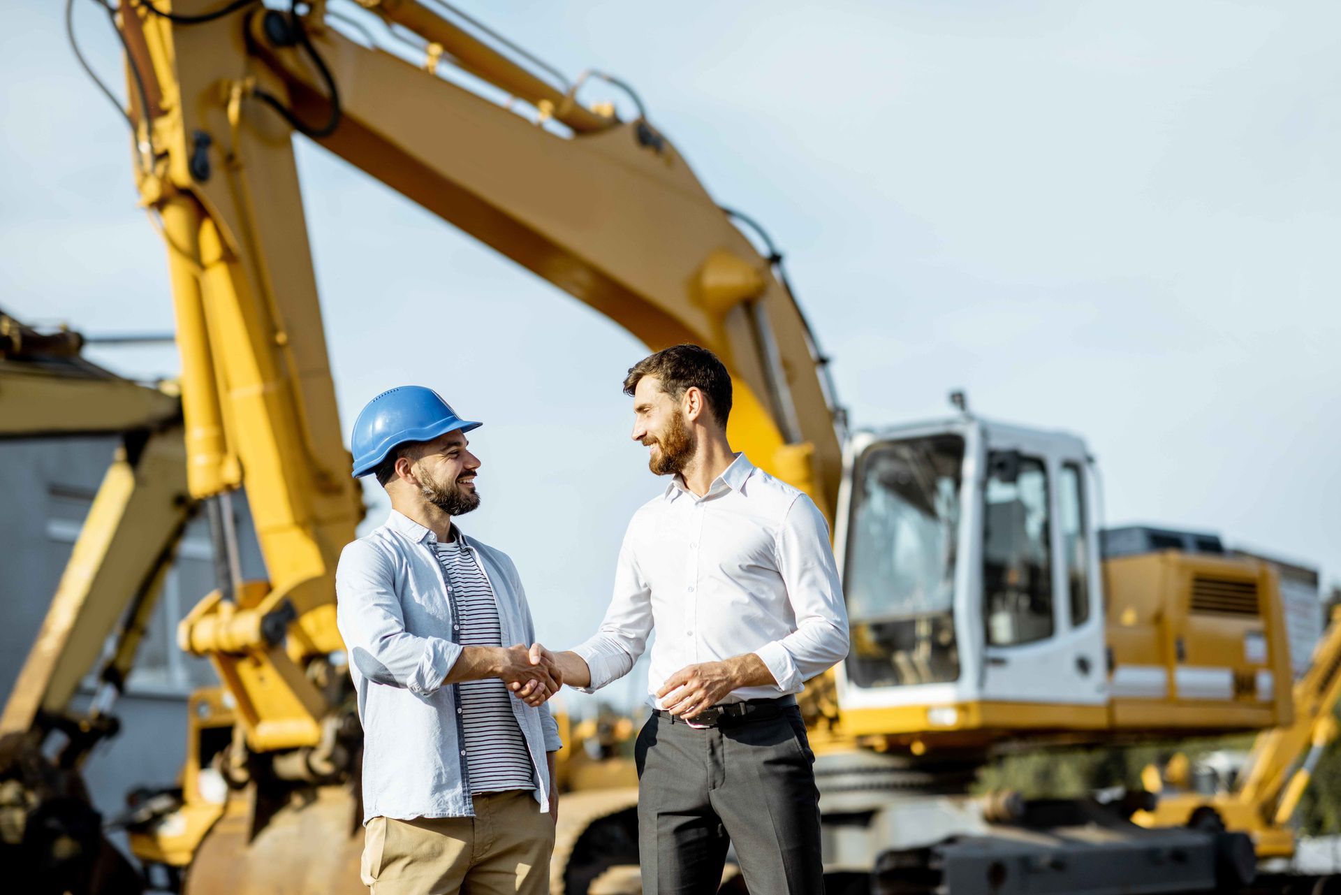 two men shaking hands in front of a yellow excavator