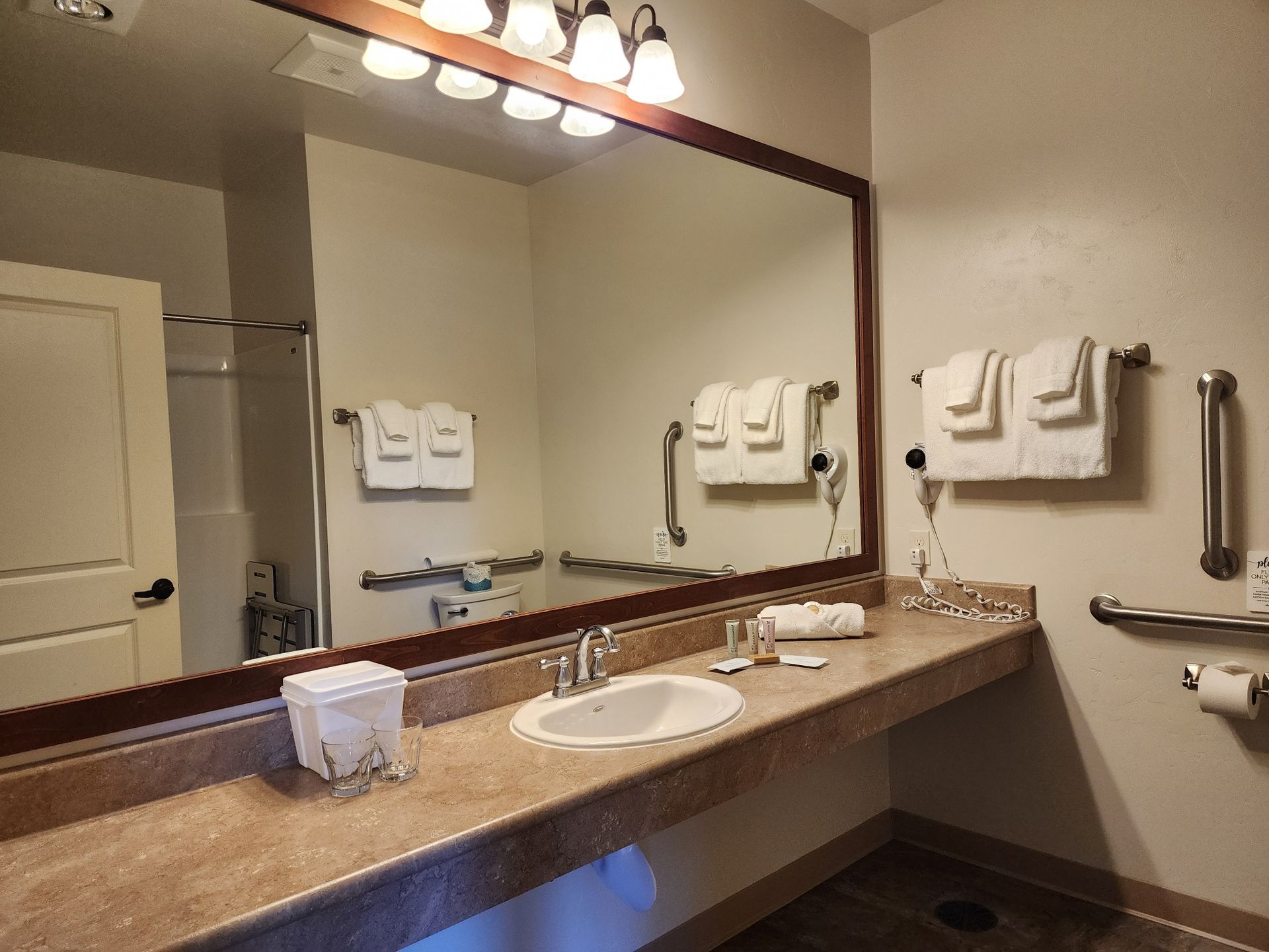 Bathroom with large mirror, accessible sink, towel rack, grab bars.