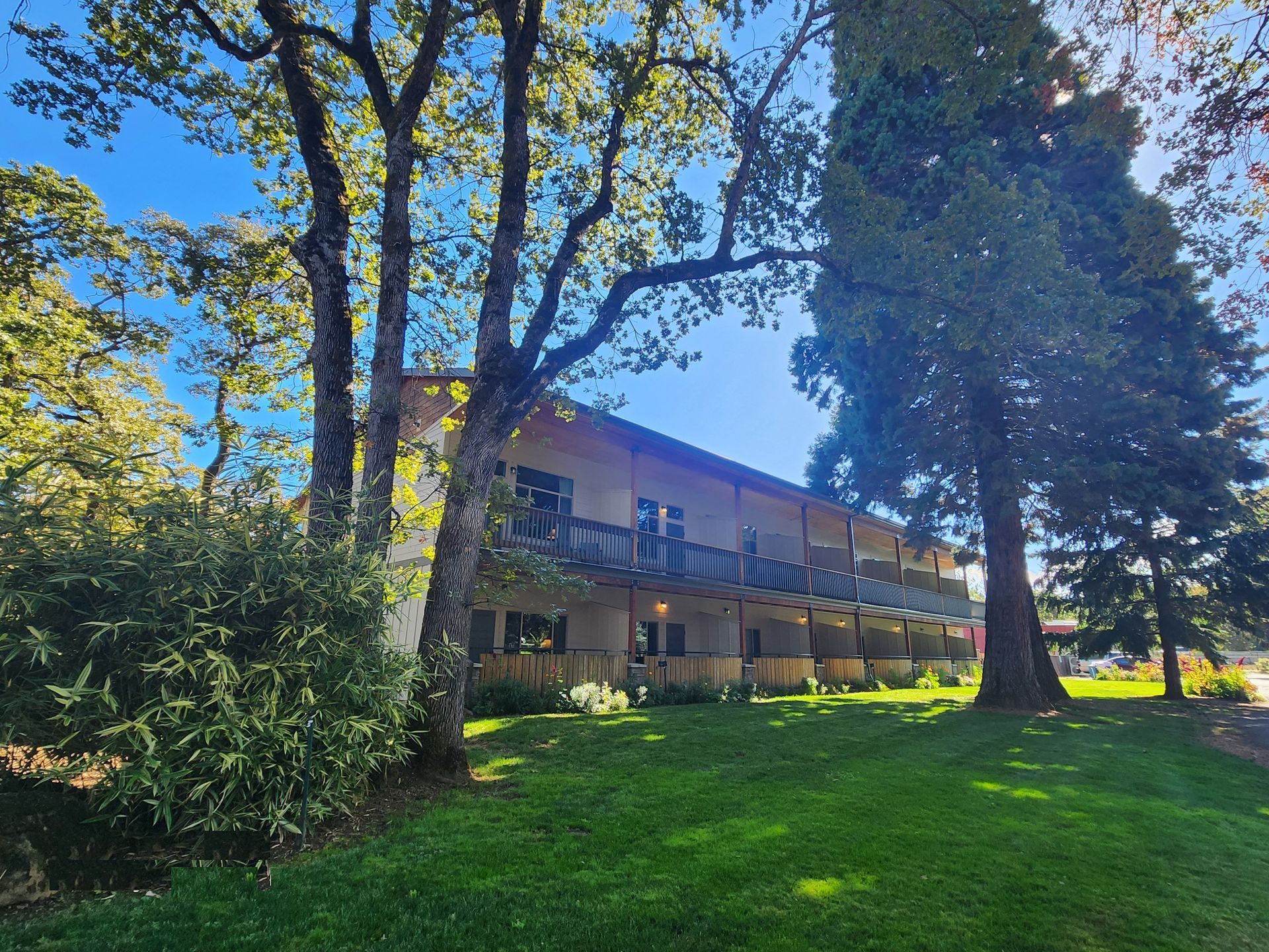 Two-story building with balconies, set among trees and green grass under a blue sky.