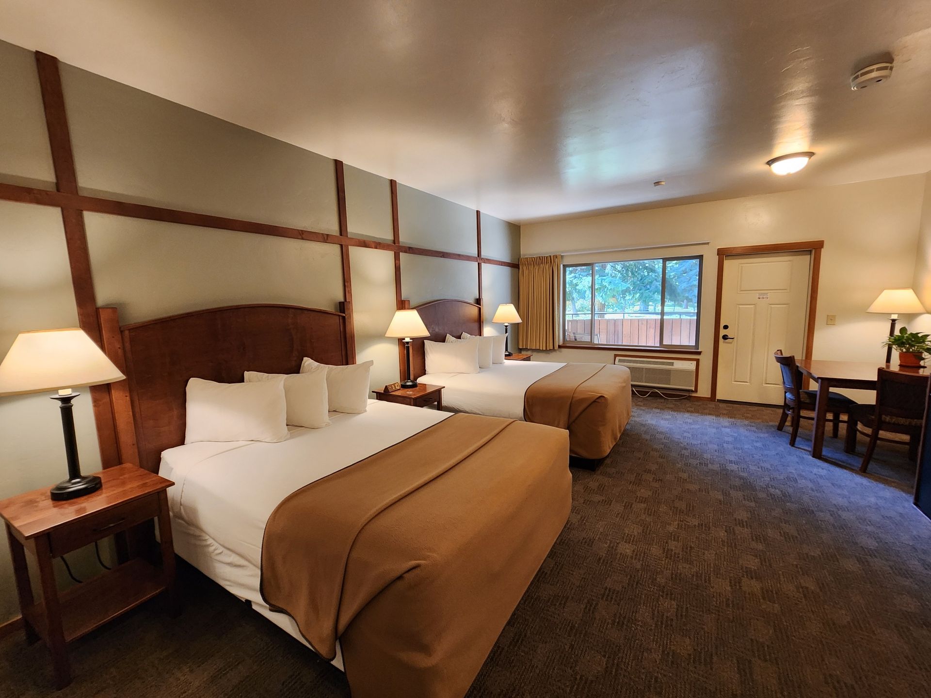 Hotel room with two queen beds, lamps, table, and chairs.