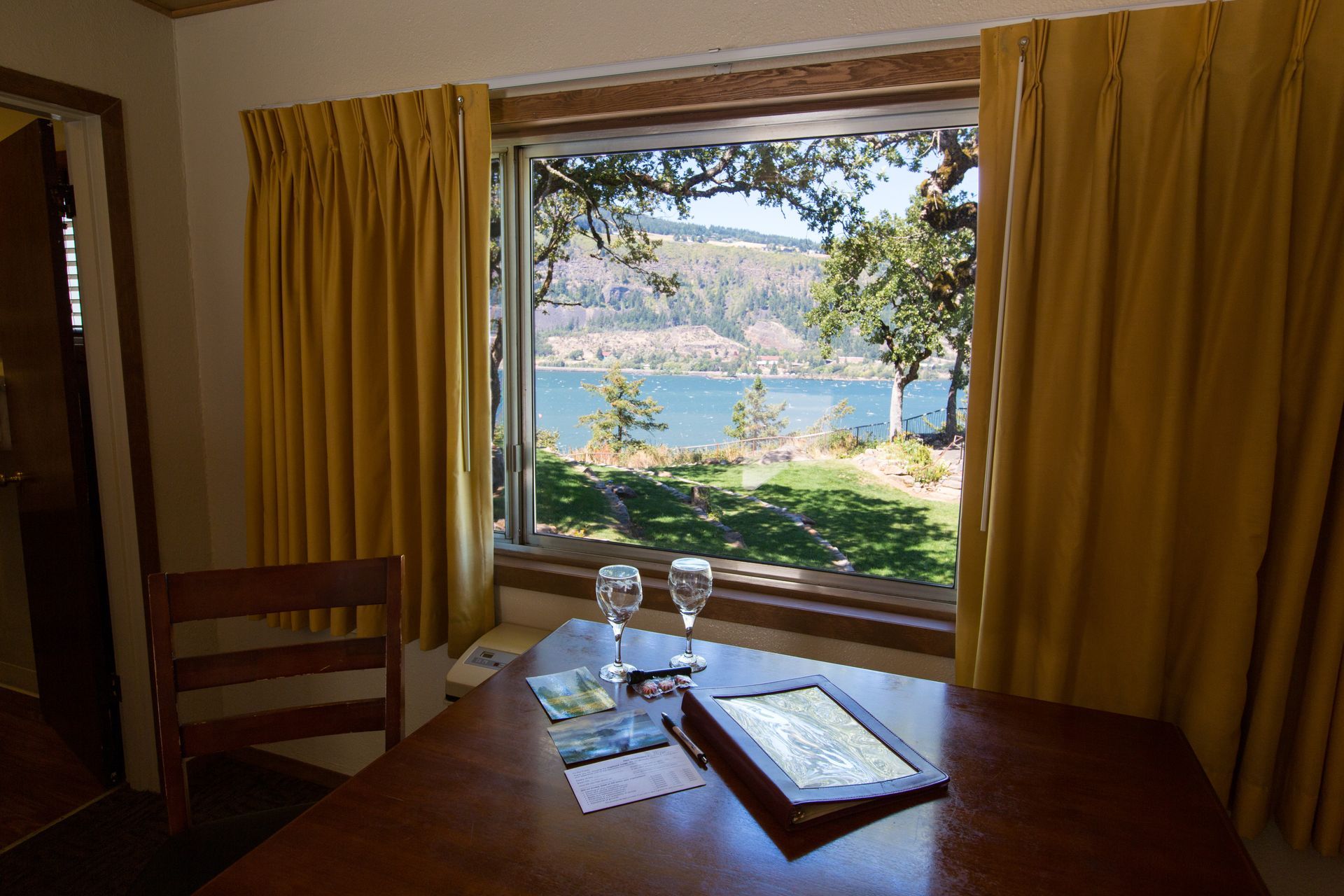 A room with a view: a table with champagne glasses and a map sits before a window overlooking a river and trees.