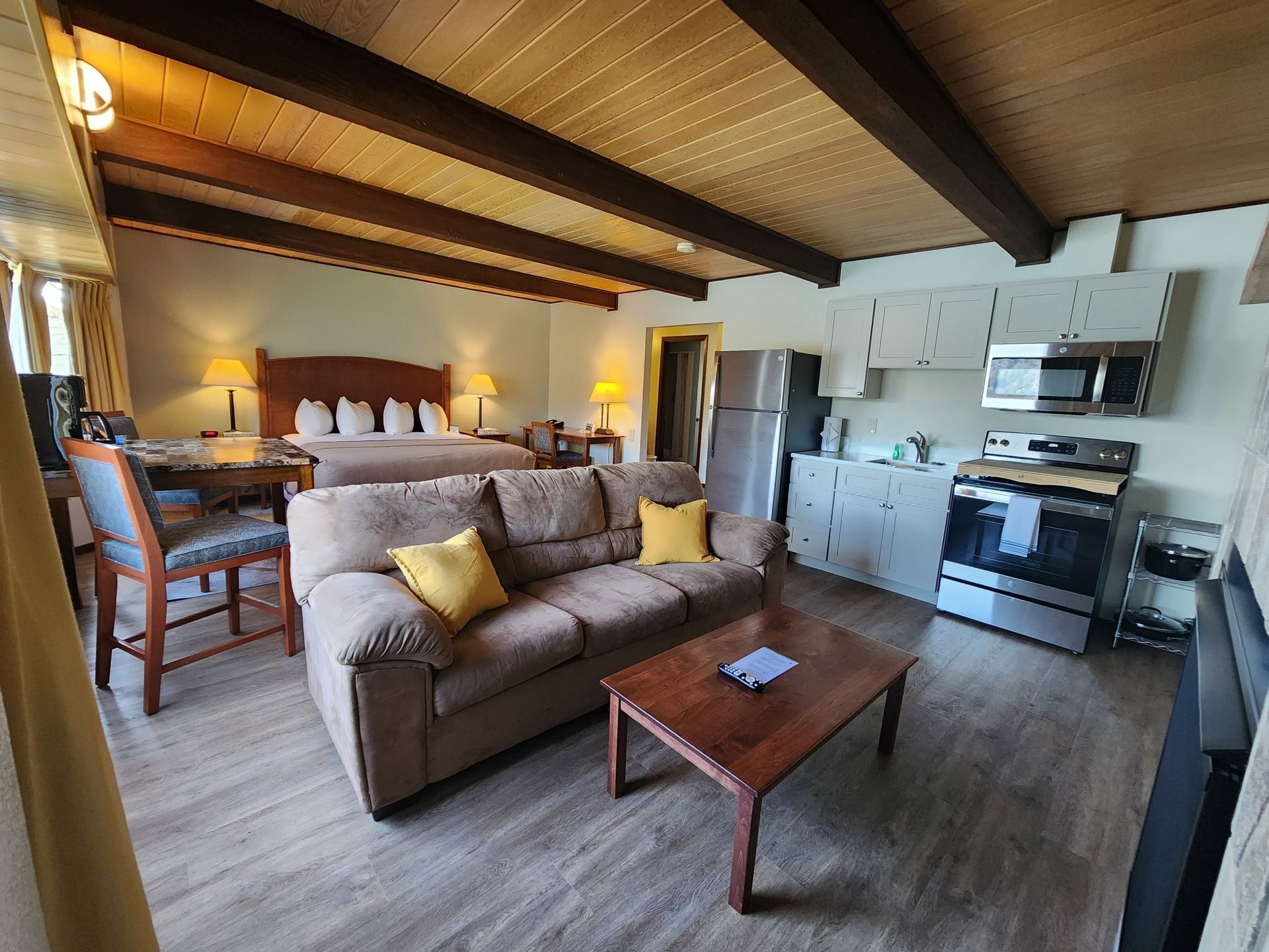Cozy hotel room with a bed, sofa, kitchenette, and wood beam ceiling.