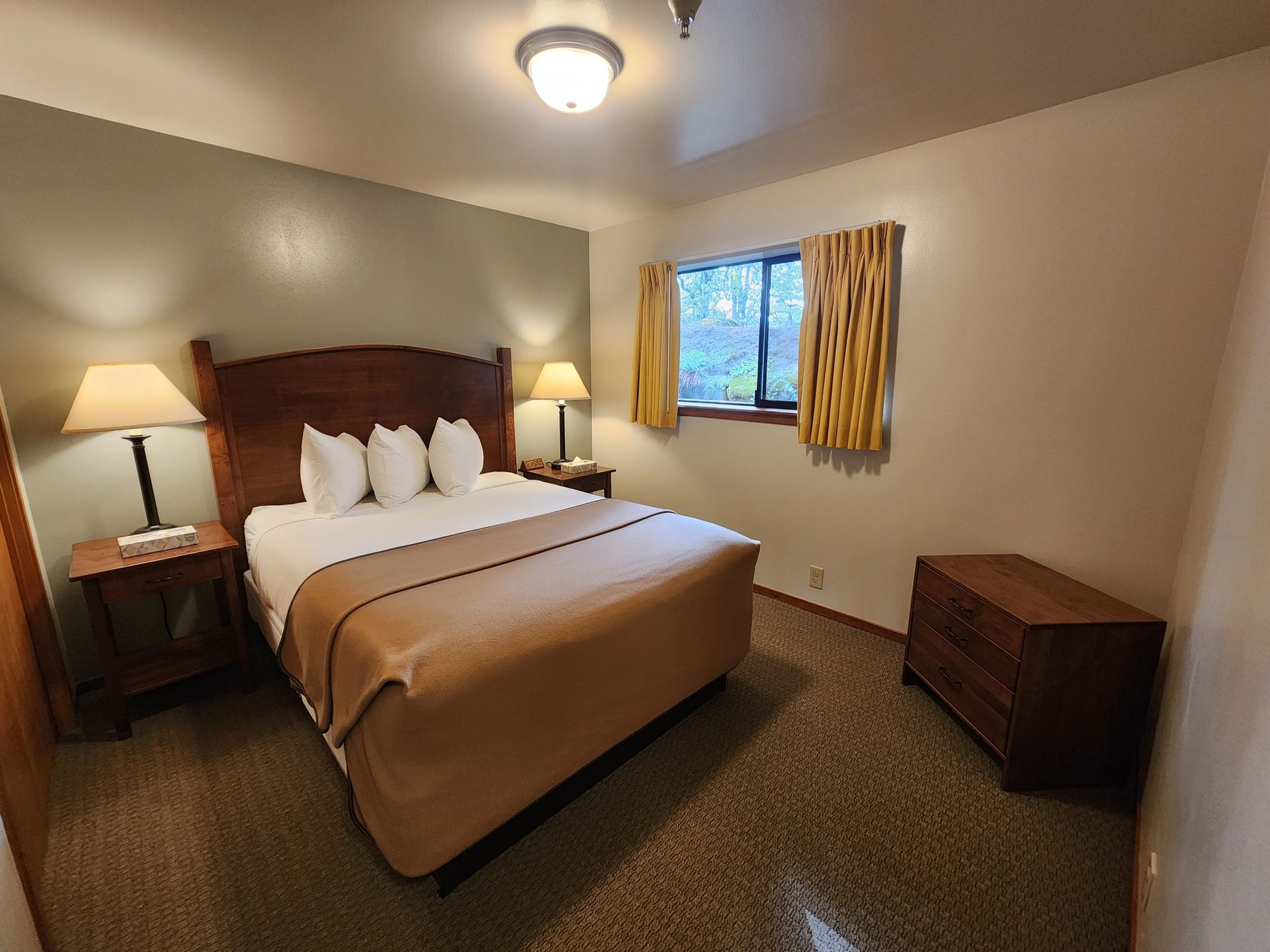 Bedroom with a bed, nightstands, lamps, a dresser, and a window with yellow curtains.