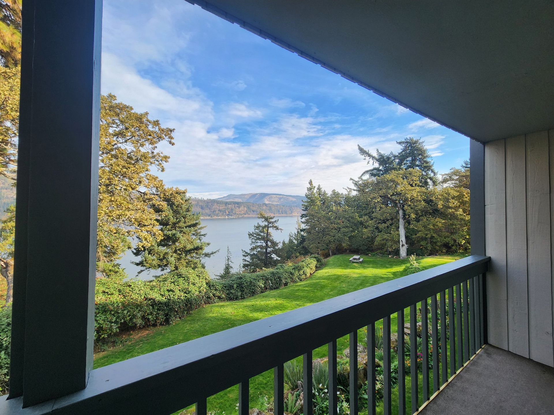 View from a balcony overlooking a body of water with trees, grass, and a blue sky.