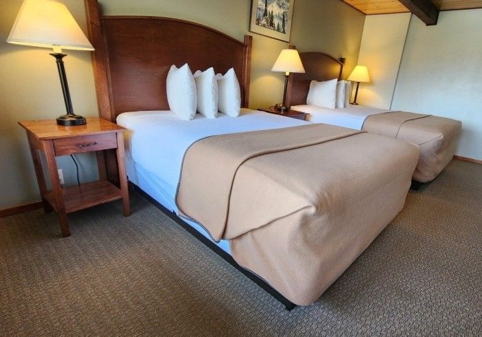 Two beds in a hotel room with tan blankets, nightstands, and lamps.