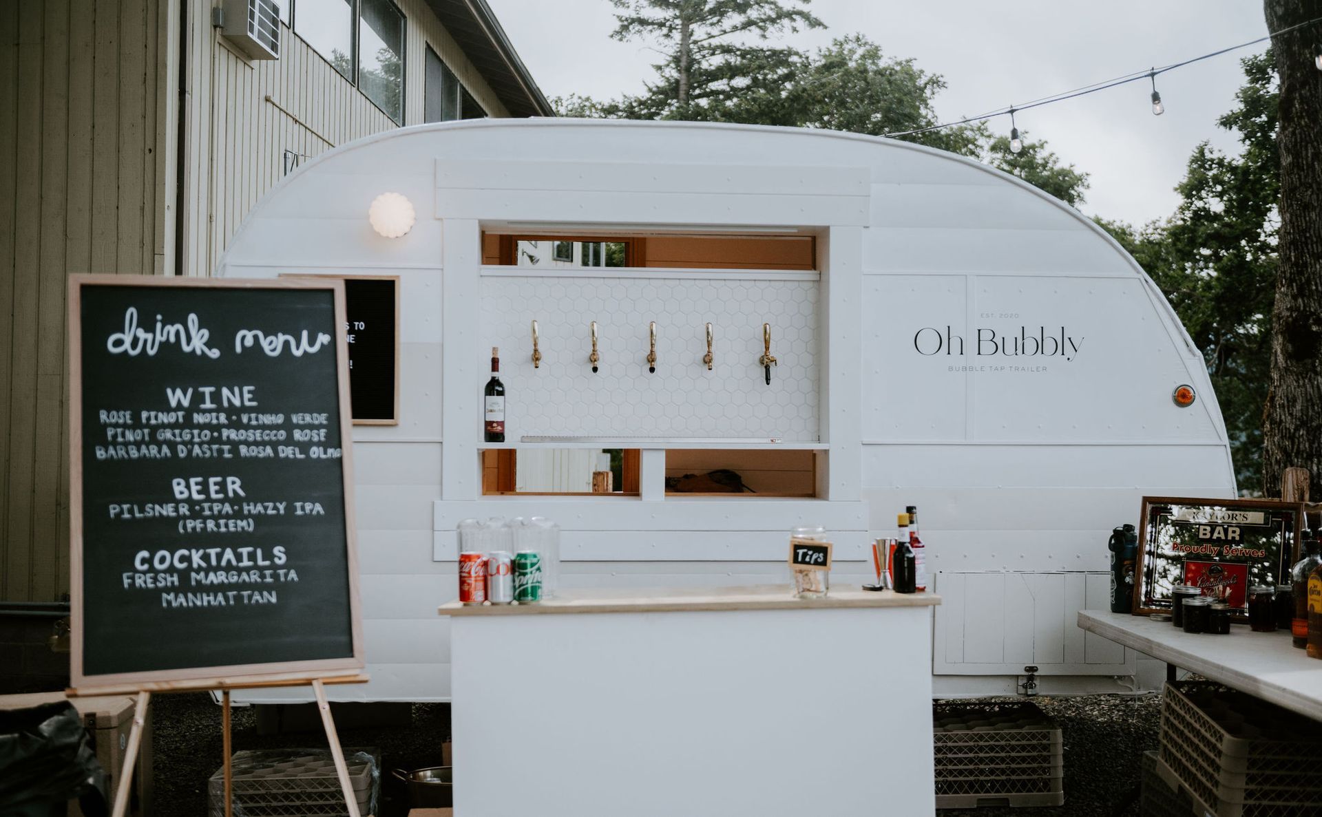 White vintage camper turned bar with a drink menu on an easel.